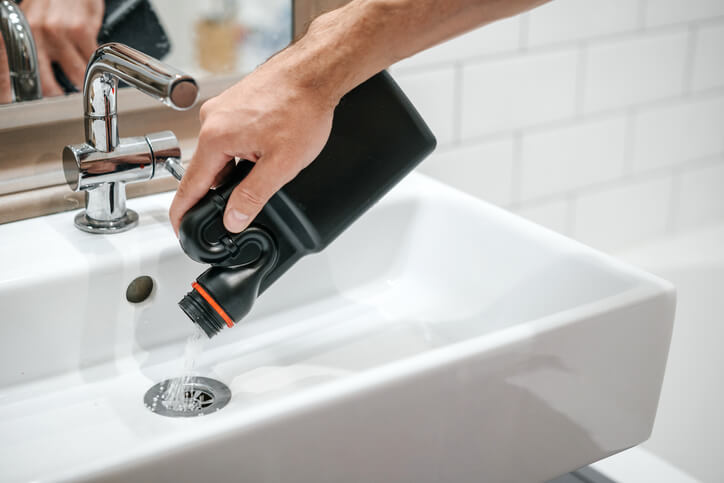 Someone using drain cleaner to unblock a bathroom sink.