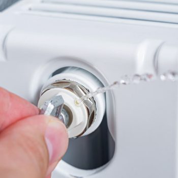 DIY Radiator bleeding: How to bleed a radiator. Close up of a hand using a radiator bleed key to bleed a radiator.