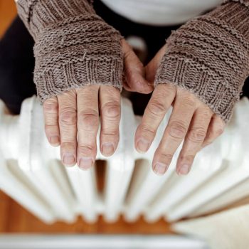 How to keep your house warm in winter: 13 easy changes Woman warming her hands on a radiator with knitted fingerless gloves