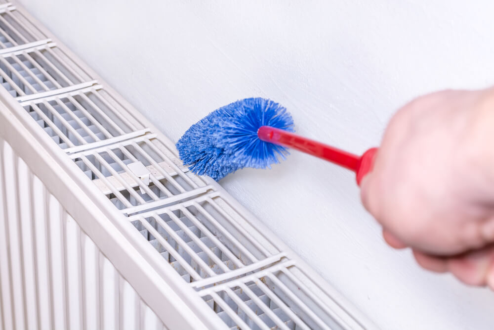 Close up of someone cleaning behind a radiator